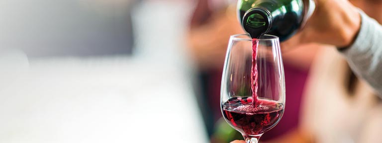 A person pouring red wine from a bottle into a glass